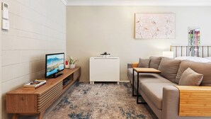 A modern living room with a sofa, a TV on a wooden stand, a white radiator, and a large abstract painting on the wall. - Comfy Studio Near Gabba With Secure Parking (Brisbane)
