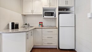 A modern kitchen with white cabinets, a microwave, a refrigerator, and a sink. - Comfy Studio Near Gabba With Secure Parking (Brisbane)
