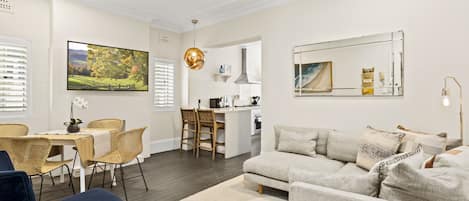 A modern living room with a sofa, a dining table with chairs, a kitchen area, and a large mirror.