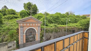 Un bâtiment doté d’une petite entrée en arc de cercle, entouré de verdure et bordé d’un mur de pierre.