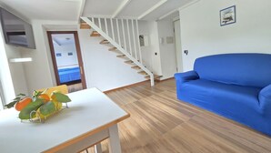 Un salon avec un canapé bleu, un parquet, un escalier et une table sur laquelle se trouvent des fruits.