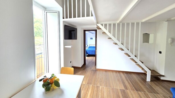 Un intérieur moderne avec un escalier, un coin repas comprenant une table et des chaises, et une vue à travers une porte vitrée.