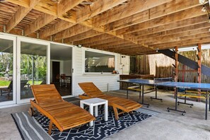 Un patio al aire libre con mesa de ping pong, dos sillones de descanso y una mesita.