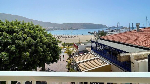 A coastal view with a beach, a clear sky, and a building with a red-tiled roof. - Arco Nº 6 - nice studio in first line to the sea (Playa De Los Cristianos)