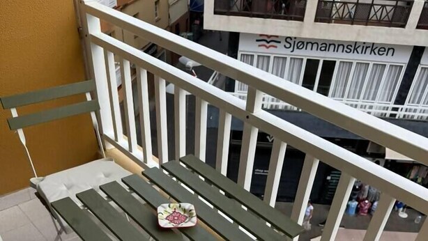 A balcony with a table and a cushioned chair, a small decorative item on the table, and a view of a building with a sign reading "Sjomansskirken". - Don Diego - 2 bedroom in front of the beach (Playa De Los Cristianos)