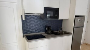 A compact kitchen with white cabinets, a black microwave, a stainless steel refrigerator, and a coffee maker. - Don Diego - 2 bedroom in front of the beach (Playa De Los Cristianos)