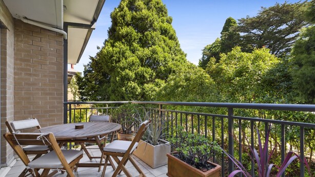 A balcony with a wooden table and chairs, surrounded by potted plants and a view of a tall tree. - Spacious 2-bed Apartment in Heart of Leura (Leura)
