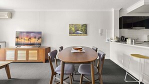 A modern kitchen with white cabinets, a wooden dining table with six chairs, and a painting of a sunset on the wall. - Spacious 2-bed Apartment in Heart of Leura (Leura)