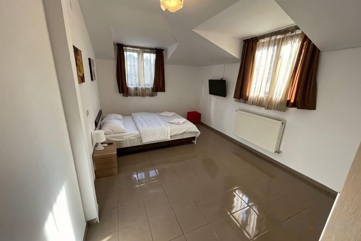 A bedroom with a bed, a window, a radiator, and a television.