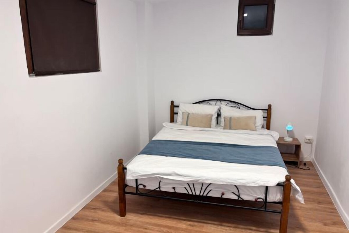 A single bed with a metal frame, a bedside table with a lamp, and a small wall-mounted shelf.