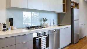 A modern kitchen with stainless steel appliances, a dishwasher, and a built-in oven. - Oceanfront 2-bed With Balcony & Study Nook (Geelong)