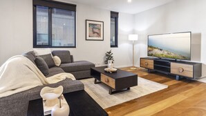 A modern living room with a sectional sofa, a flat-screen TV, and a coffee table. - Oceanfront 2-bed With Balcony & Study Nook (Geelong)