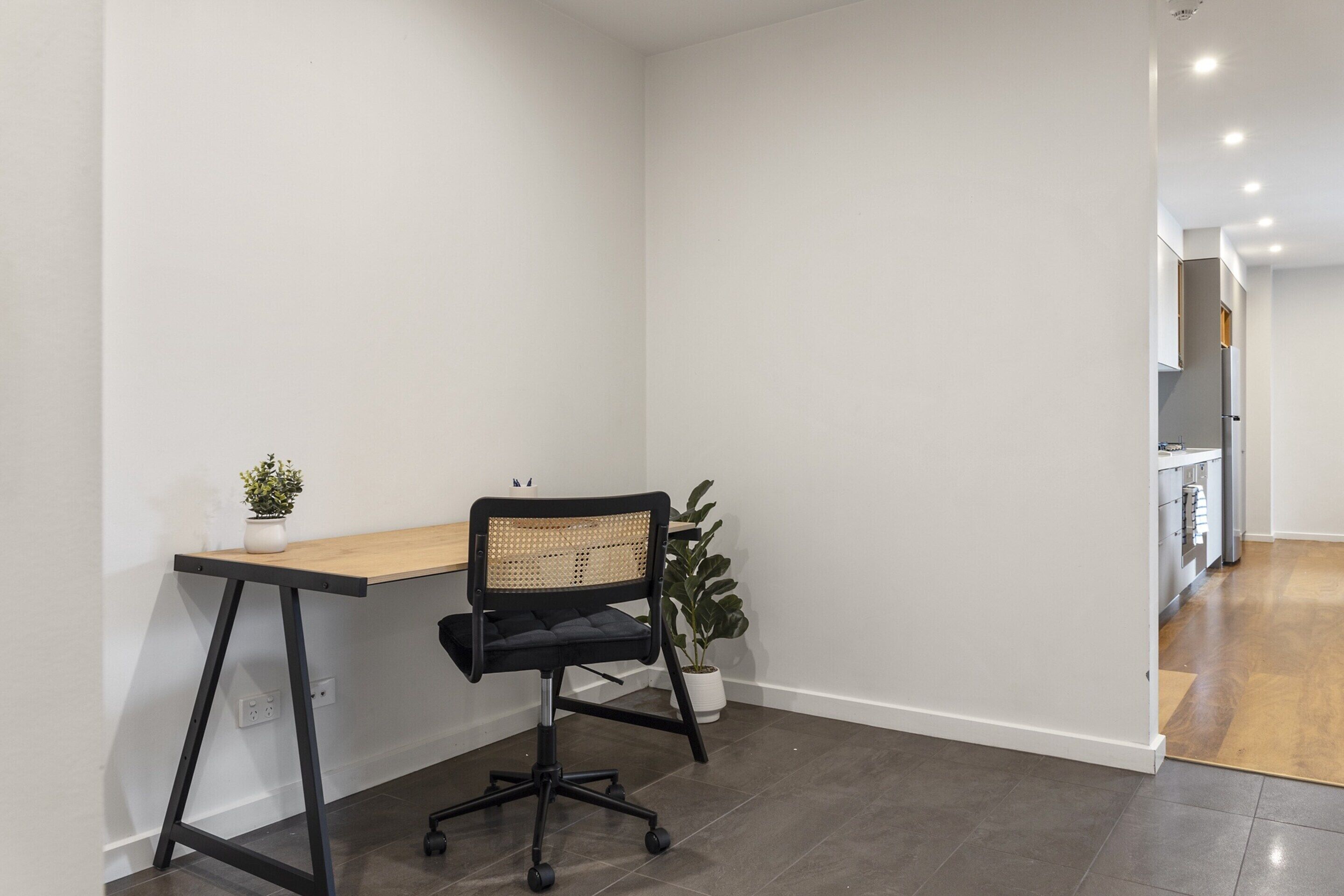 Een moderne kantoorruimte met een houten bureau, een zwarte bureaustoel en potplanten.