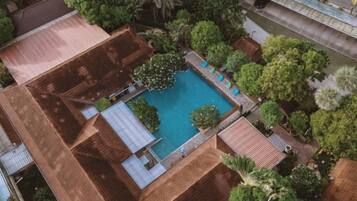 An aerial view of a property with a swimming pool surrounded by trees and a building with a tiled roof.