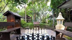 A chessboard set outdoors surrounded by wooden structures and lush greenery.