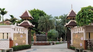 A gated entrance with traditional architectural elements, a sign reading "Villa Wanida," and a pathway leading into a lush, green area.