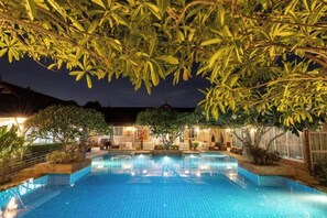 A swimming pool with tiled flooring, surrounded by trees and a building with illuminated windows. - Villa Wanida Garden Resort (Pattaya)