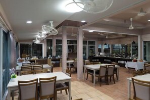 A restaurant with multiple dining tables and chairs, a kitchen area, and large windows. - Villa Wanida Garden Resort (Pattaya)