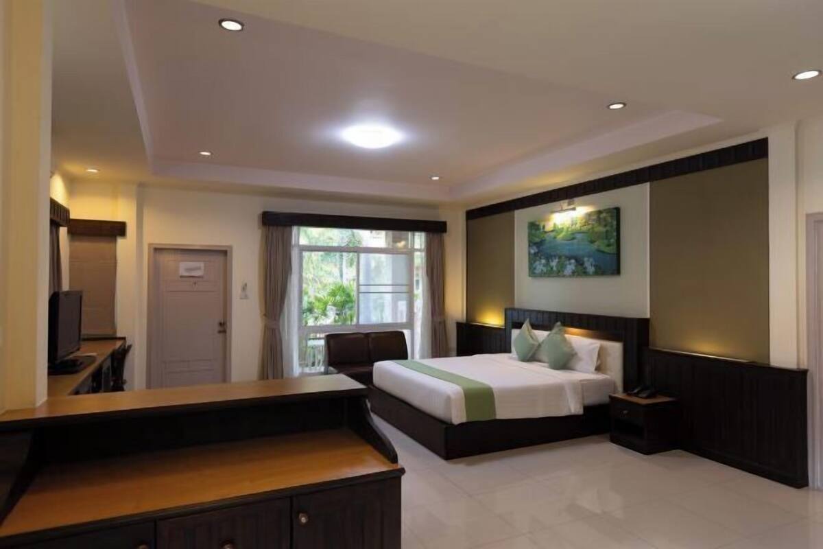 A hotel room with a bed, a desk, a chair, a TV, a window, and a painting on the wall.