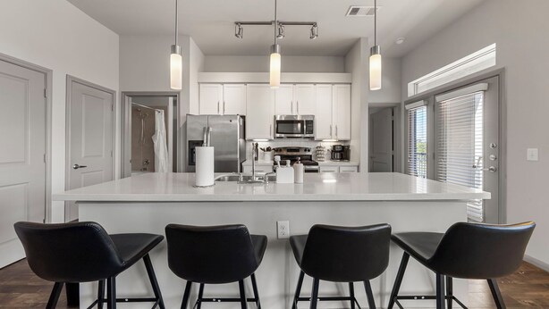A modern kitchen with a large island, stainless steel appliances, and black bar stools. - Charming 2-bedroom apartment with Pool, Gym. Close to Dwtn & Airport (Austin)