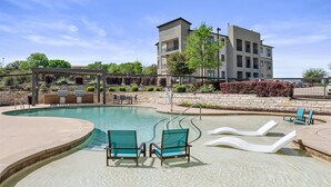 A swimming pool with lounge chairs, a pergola, and a building with multiple floors and balconies. - Charming 2-bedroom apartment with Pool, Gym. Close to Dwtn & Airport (Austin)