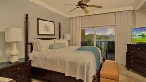 A bedroom with a bed, a ceiling fan, a television, a dresser, and a window with a view of a balcony. - Ritz Carlton Residence spacious 3-bedroom beach front condo with best dates! (St Thomas)