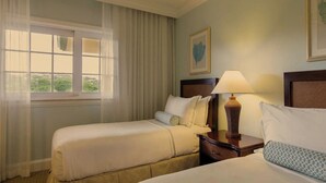 A hotel room with two beds, a window with curtains, a ceiling fan, a nightstand with a lamp, and a framed picture on the wall.