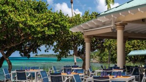 An outdoor dining area with tables and chairs, overlooking a clear blue sea.