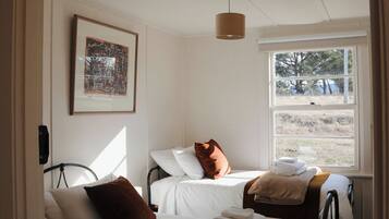 A room with a bed, a window with a view of trees, a hanging light fixture, and a framed picture on the wall.