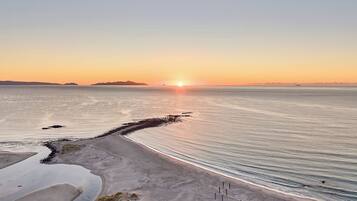 A beach with a clear sky, calm sea, and distant land.