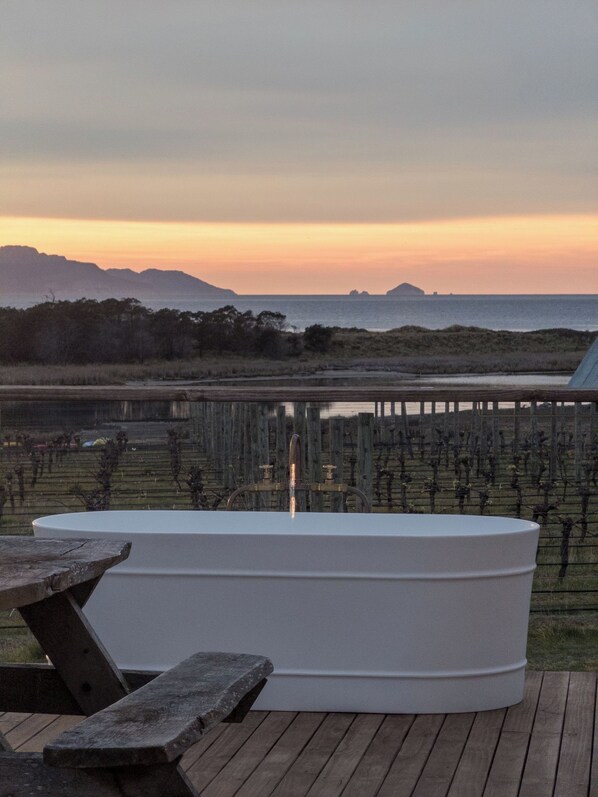 A wooden deck with a hot tub and picnic tables overlooking a body of water with distant landforms.
