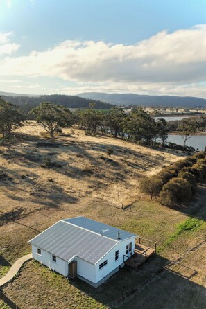 A single-story white house with a sloped roof, situated on a grassy hill with a view of a lake and distant hills.
