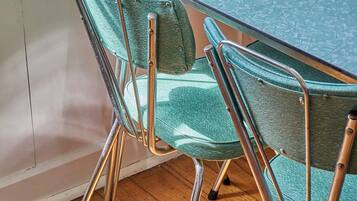 A dining table with a teal tablecloth, two chairs with green upholstery, and a stack of plates on the table.