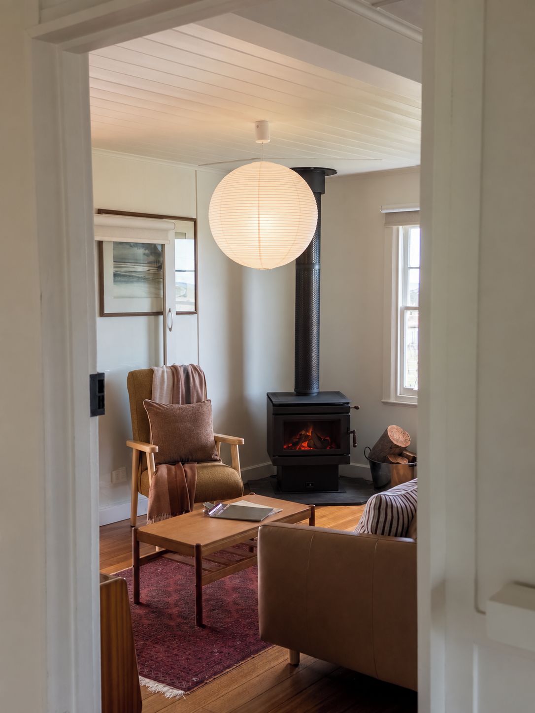 A cozy living room with a fireplace, a comfortable sofa, a wooden coffee table, and a hanging light fixture.