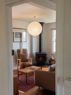 A cozy living room with a fireplace, a comfortable sofa, a wooden coffee table, and a hanging light fixture.