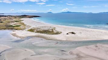 A beach with clear water, distant mountains, and a clear sky.