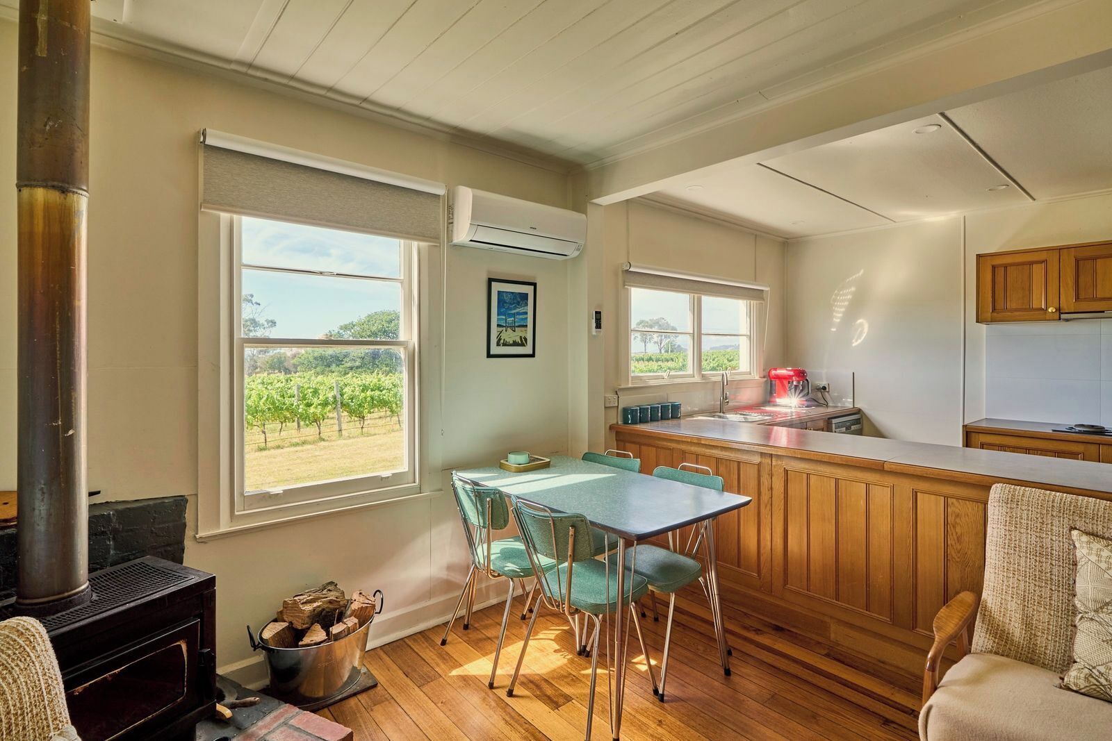 Une cuisine dotée d’un plan de travail en bois, un coin repas avec une table et des chaises, et une grande fenêtre donnant sur un vignoble.