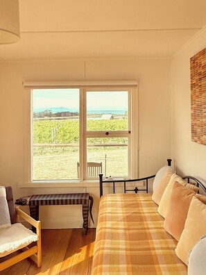 A room with a bed, a bench, and a window with a view of a vineyard and mountains.