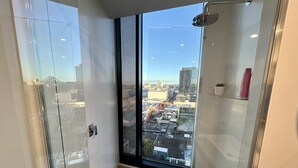 A modern bathroom with a glass door, a shower, and a view of the cityscape. - Stylish 1-bed With Pool, Gym & Free Parking (Brisbane)