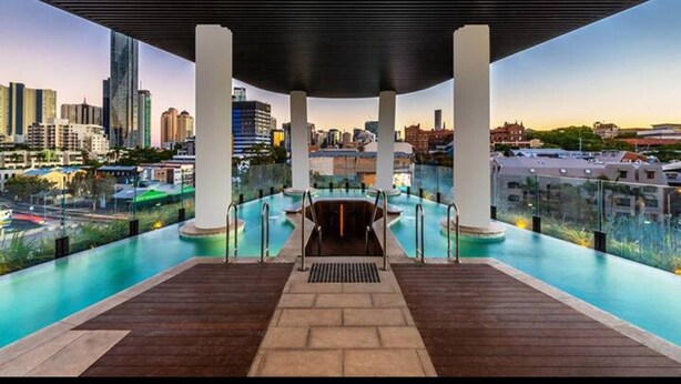 An infinity pool with a city view, surrounded by columns and a covered area. - Stylish 1-bed With Pool, Gym & Free Parking (Brisbane)
