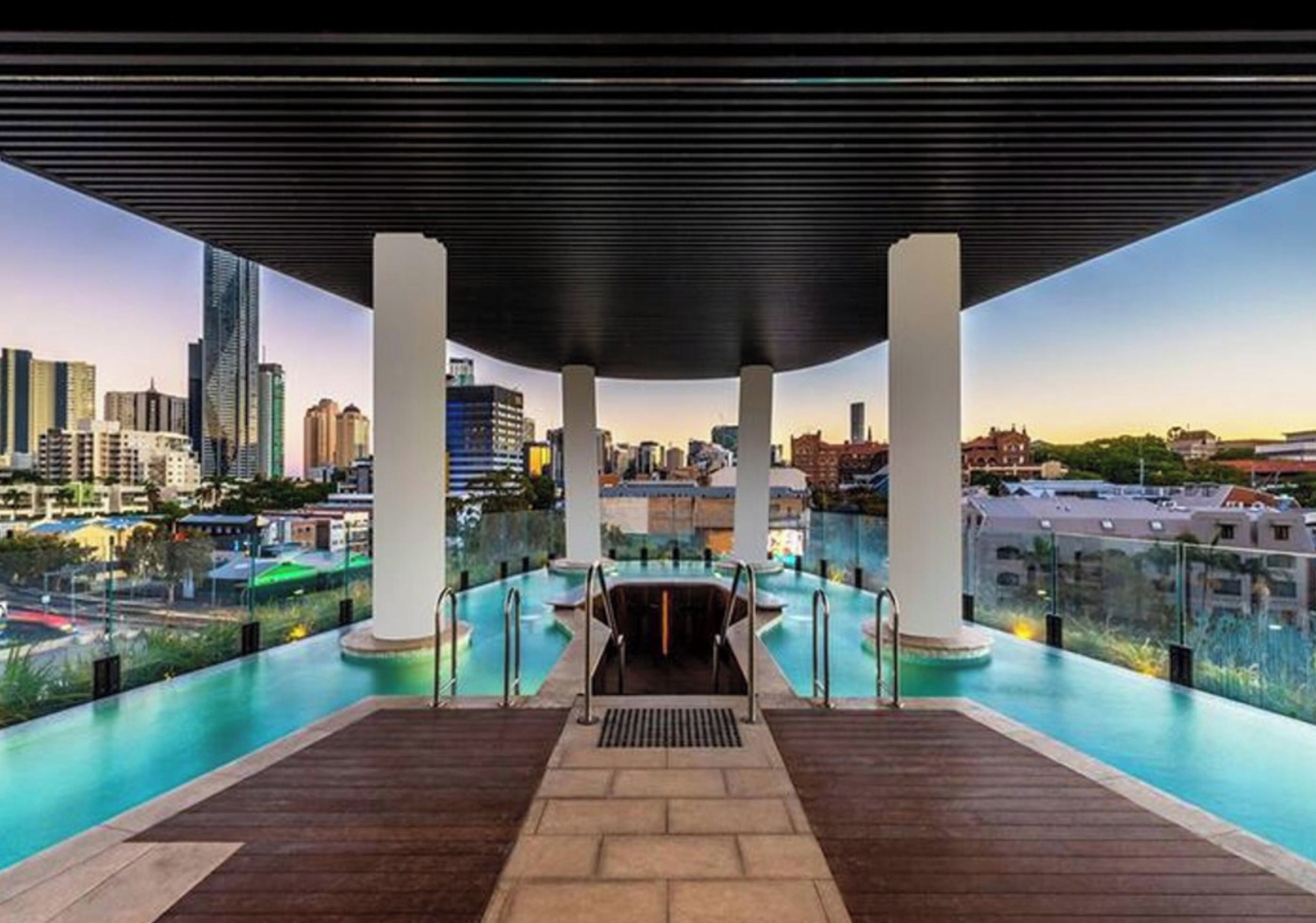 An infinity pool with a city view, surrounded by columns and a covered area.