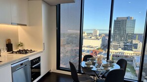 A modern kitchen with a large window, a dining area with a table set for four, and a view of the cityscape. - Stylish 1-bed With Pool, Gym & Free Parking (Brisbane)