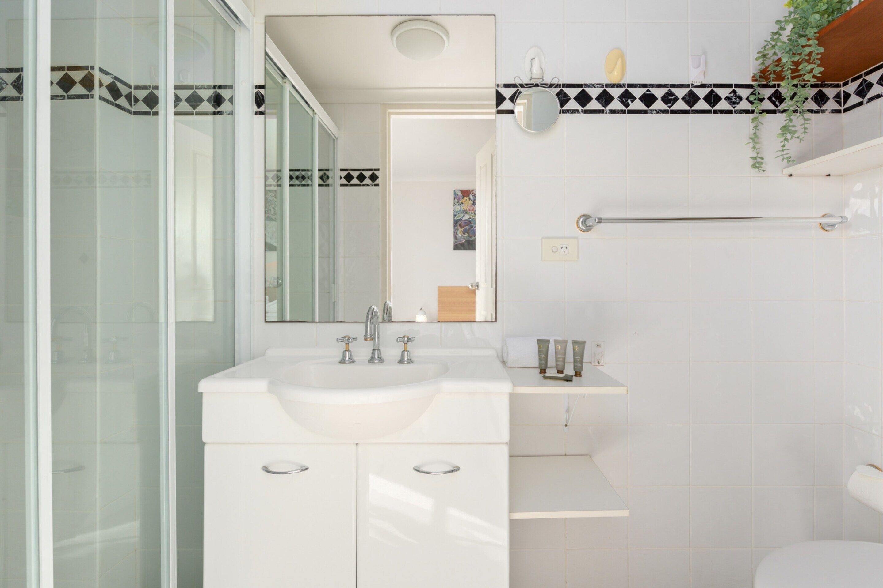Un baño moderno con cabina de ducha de vidrio, un lavamanos blanco con espejo y un perchero en la pared.