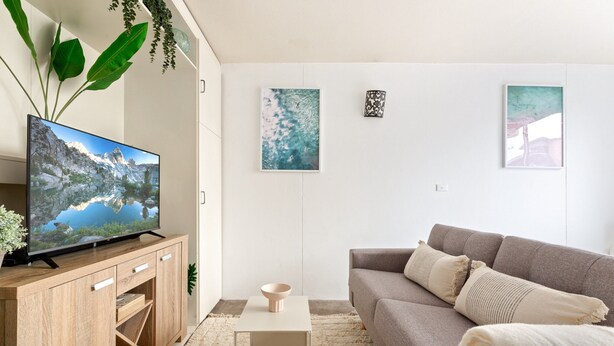 A modern living room with a flat-screen TV on a wooden cabinet, a grey sofa, a small white table, and a beige rug. - Bondi Studio Walk to Beach & Cafes (Sydney)