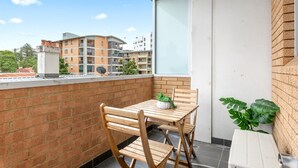 A balcony with a wooden table and chairs, a potted plant, and a view of surrounding buildings. - Bondi Studio Walk to Beach & Cafes (Sydney)