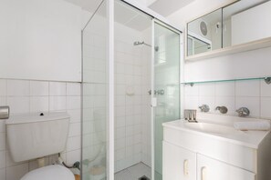 A modern bathroom with a glass shower enclosure, a white toilet, and a vanity with a mirror. - Bondi Studio Walk to Beach & Cafes (Sydney)