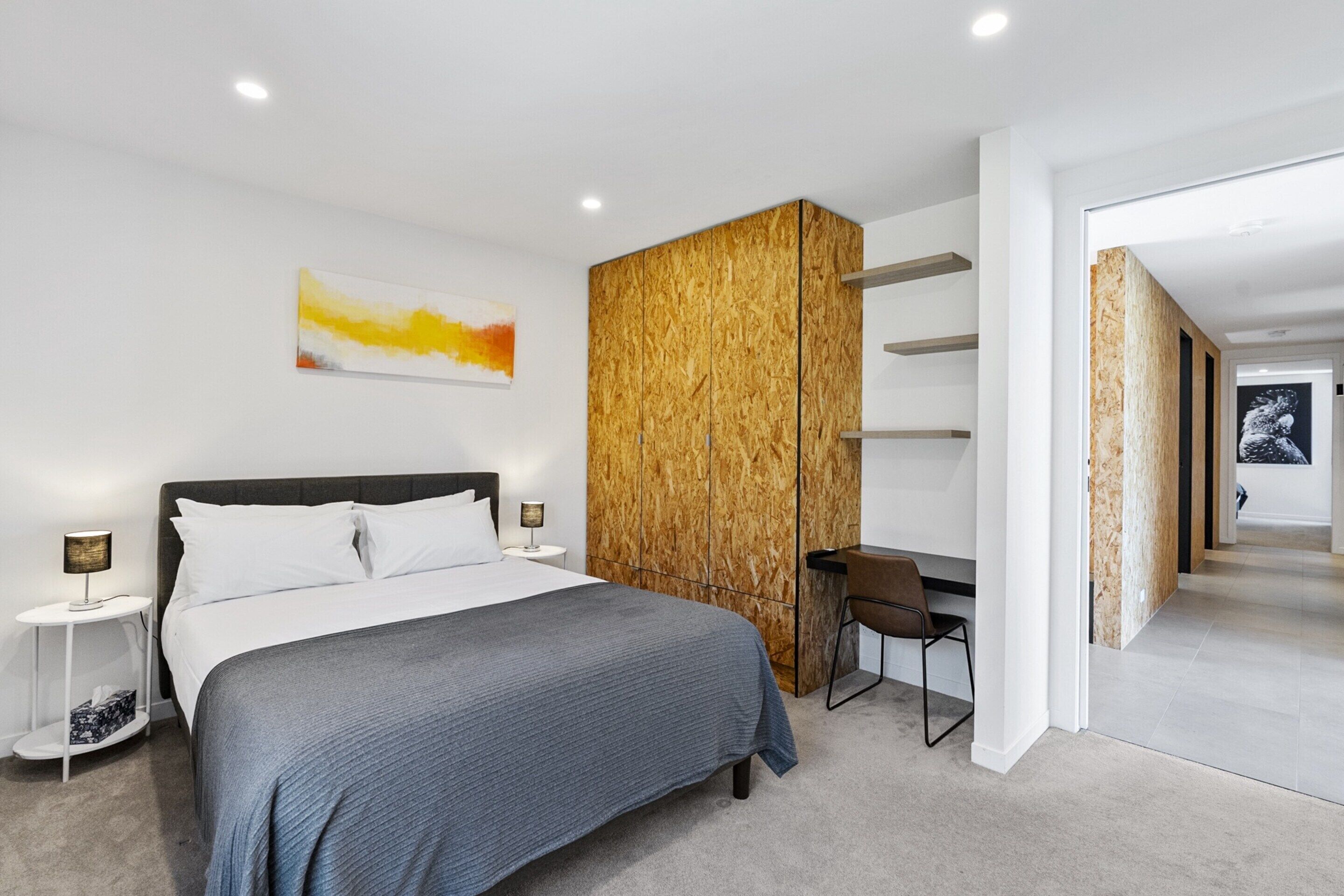 A modern bedroom with a large bed, a desk, and a wardrobe.