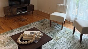 Un salon avec un ventilateur de plafond, un téléviseur posé sur un meuble en bois, une chaise blanche et une table basse agrémentée d’objets décoratifs.