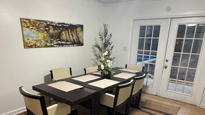 Un coin repas comprenant une table et des chaises, un ventilateur de plafond, un tableau accroché au mur et une porte à panneaux de verre.