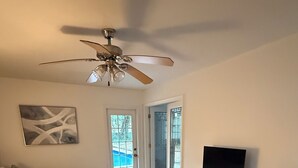 Une chambre à coucher comprenant un lit, un téléviseur, un ventilateur de plafond, un tapis à motifs et une porte donnant sur un balcon.